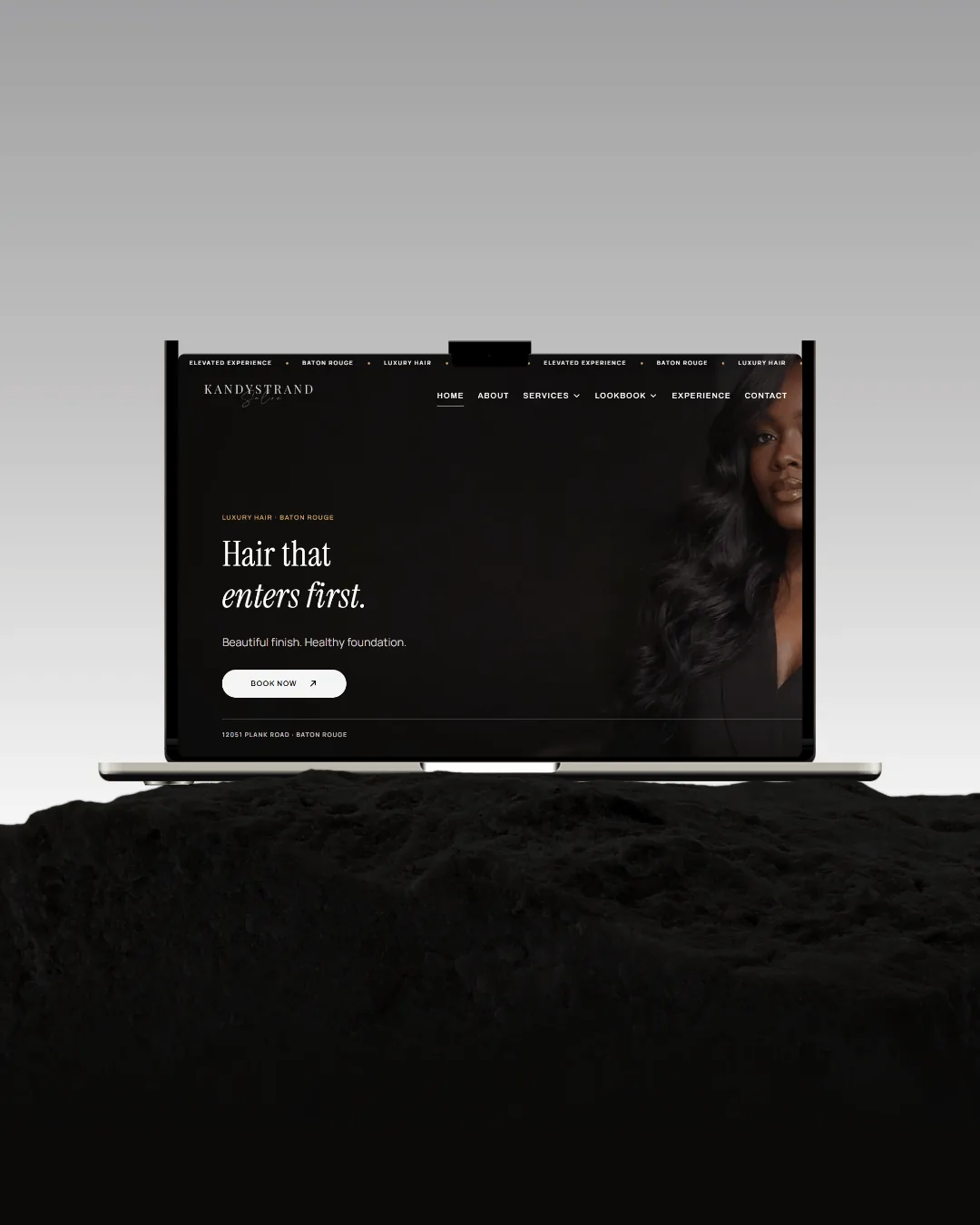 A laptop on black rock under a grey sky, the Kandy Strands homepage filling its screen — a portrait in low gold light