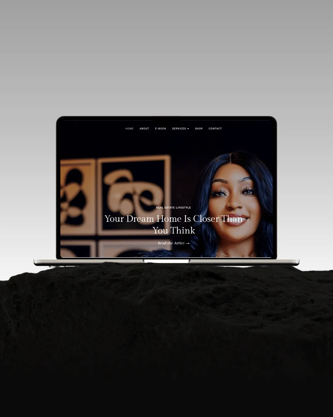 A laptop on black rock under a grey sky, showing the Keys & Coffee homepage — “Your Dream Home Is Closer Than You Think”